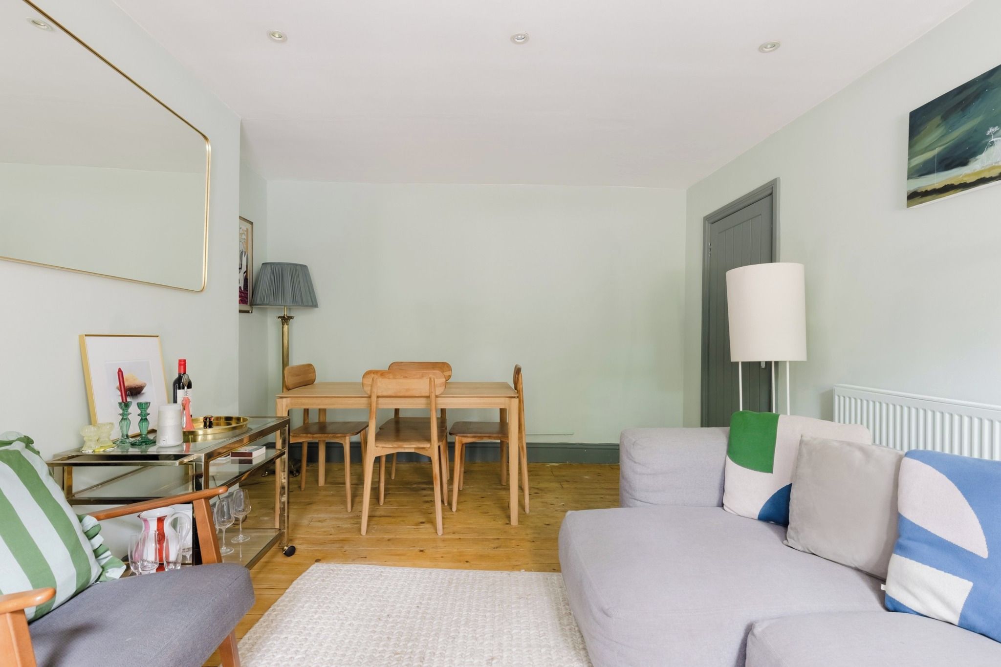 Ein Wohnzimmer mit einer Couch, einem Esstisch mit Stühlen, einer Lampe und einer Heizung.