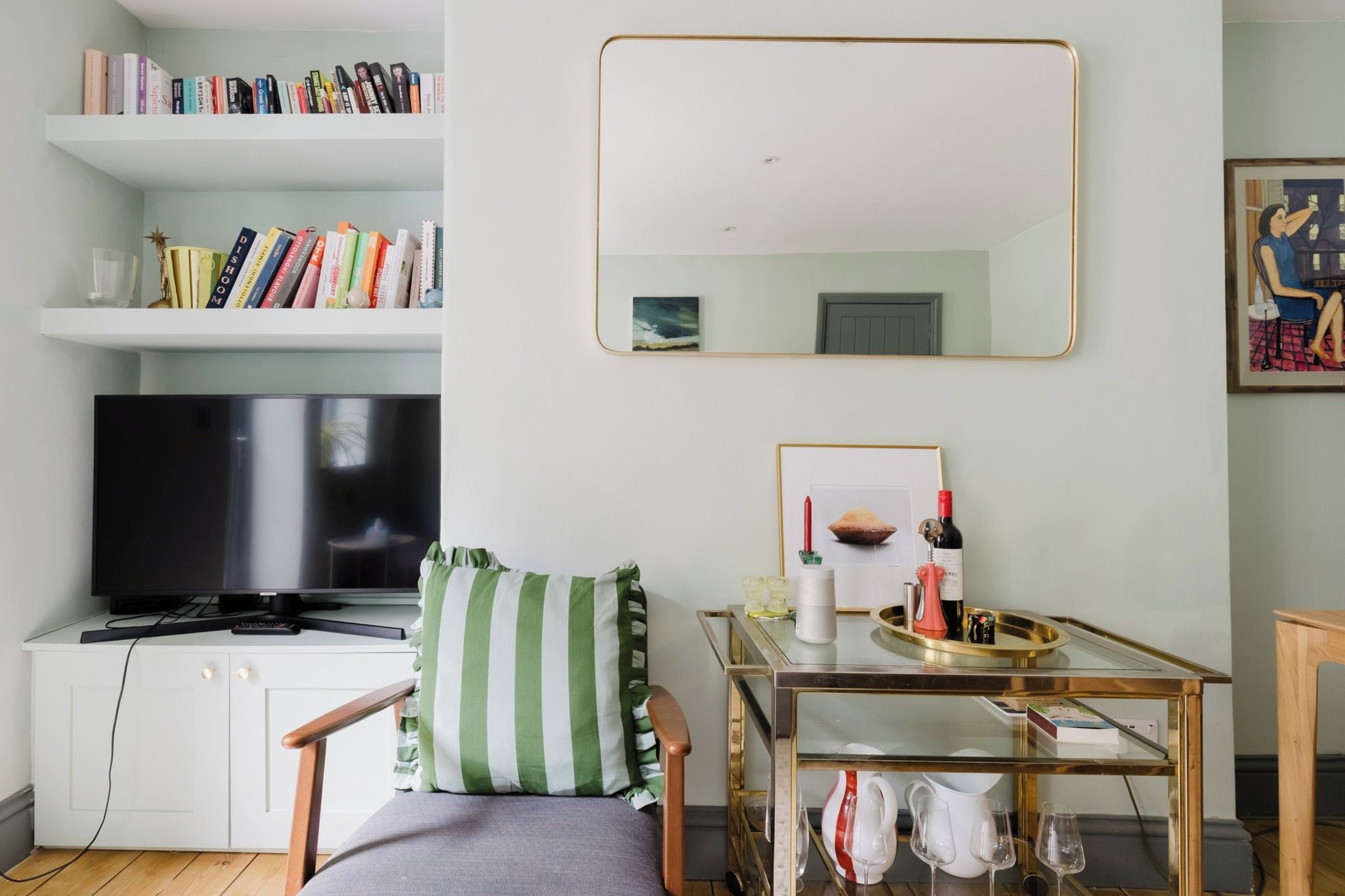 Uma sala de estar moderna com uma televisão de tela plana, uma estante, uma mesa de jantar com copos de vinho e uma cadeira com almofada listrada.