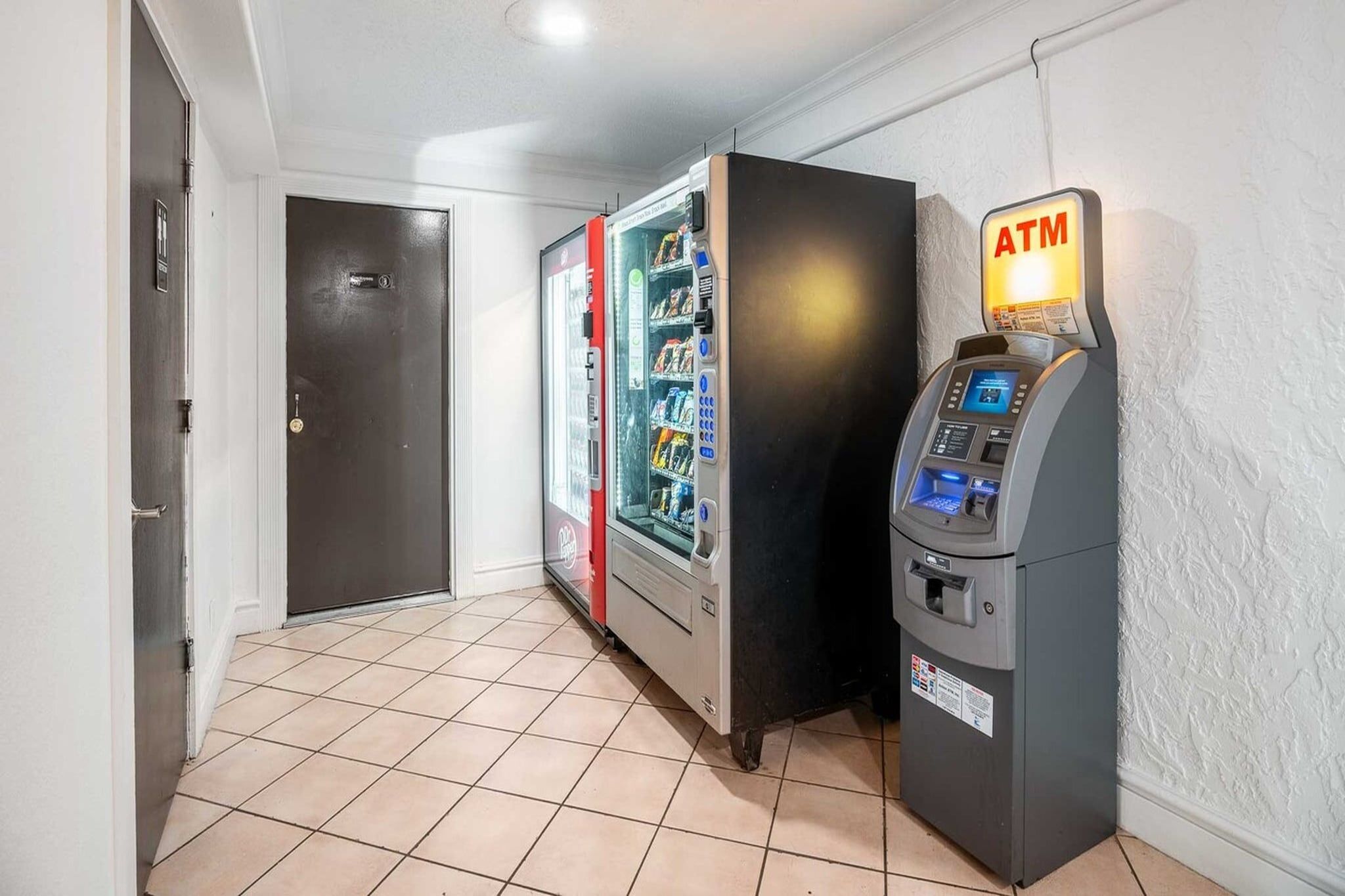 Un couloir avec un distributeur automatique, un réfrigérateur et une porte.