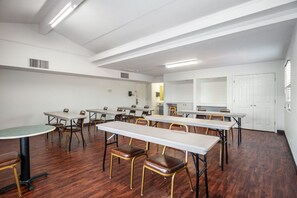 Une salle de conférence dotée de plusieurs tables et chaises, de murs blancs et d’un plancher en bois.