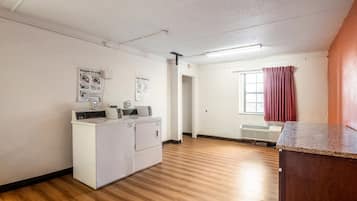 Een wasserette met een wasmachine en droger, een raam met rode gordijnen, en een deur naar een andere kamer.