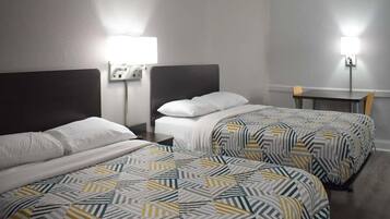 Une chambre d’hôtel avec deux lits, chacun recouvert d’une couvre-lit à motifs, une table de chevet avec une lampe et une petite table avec une chaise.