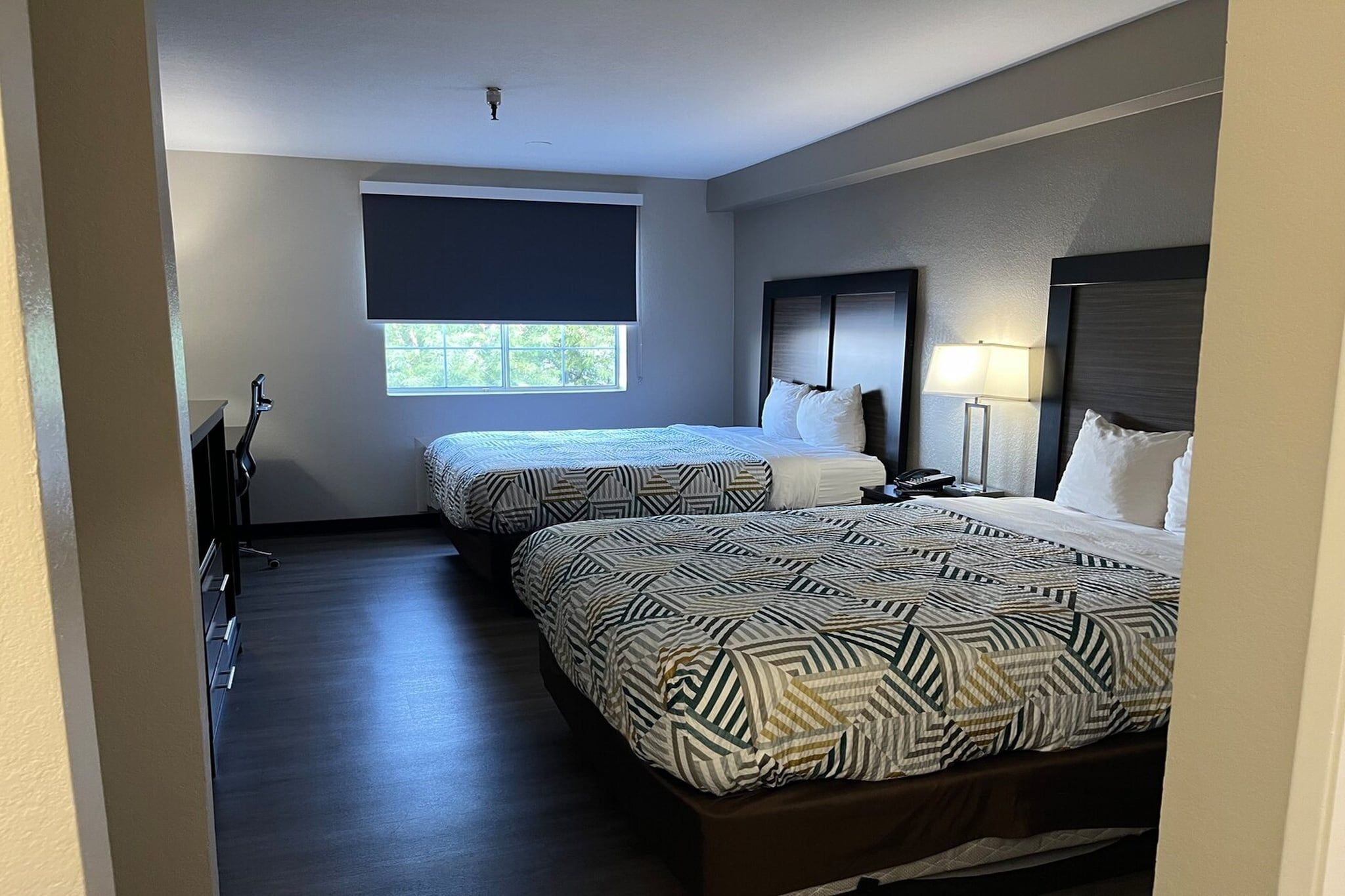 Une chambre d’hôtel avec deux lits, une fenêtre, un bureau et une lampe.