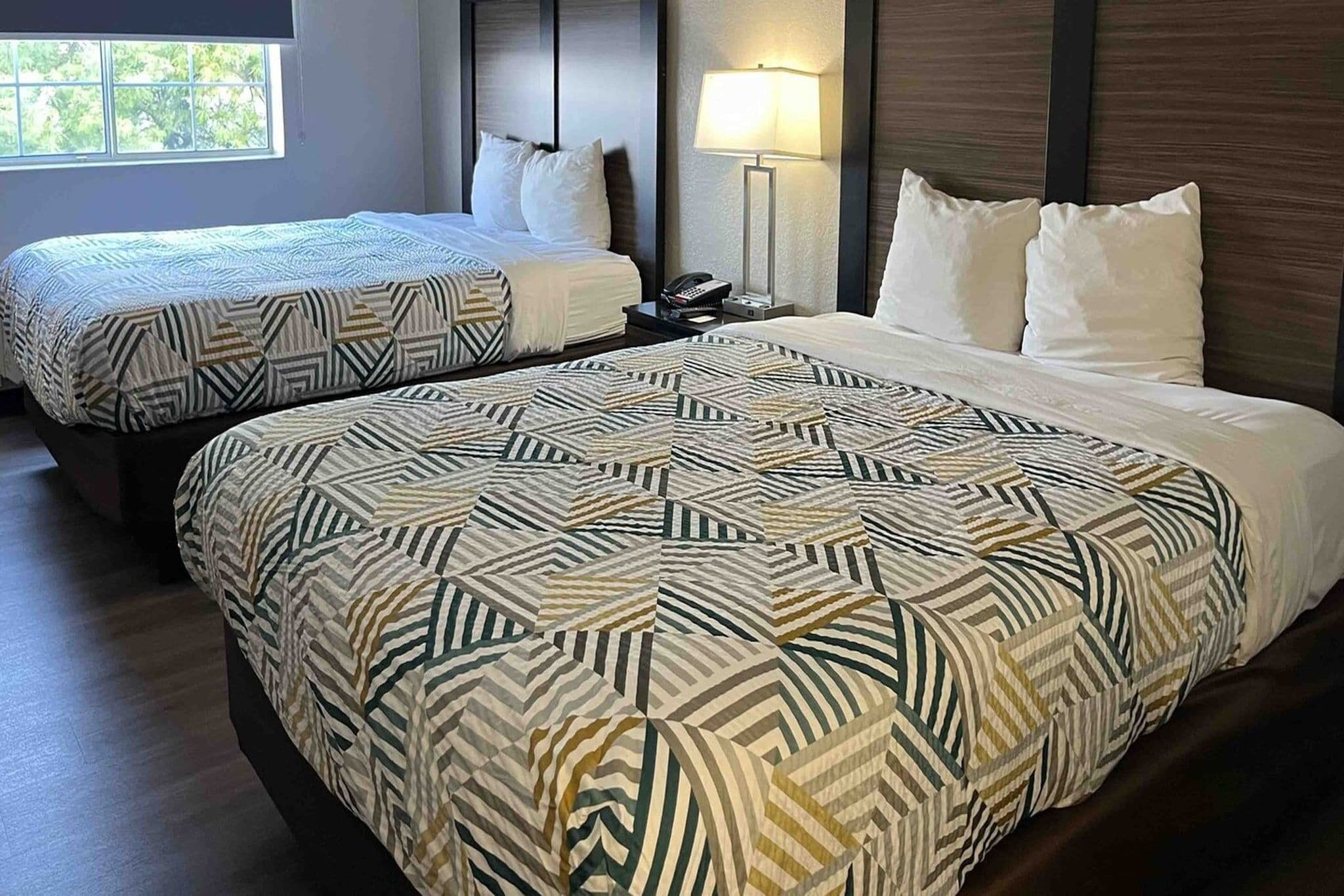 A hotel room with two beds, each with patterned bedding, a bedside lamp, and a telephone on the nightstand.
