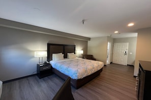 A hotel room with a large bed, two bedside tables with lamps, a chair, and a door. - 1 King Bed | Non-Smoking, Micfridge (Tucson AZ)