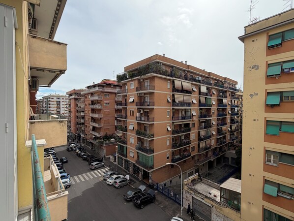 A multi-story residential building with balconies, a parking area, and a street view.