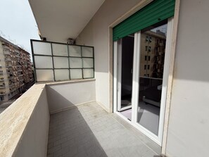 A balcony with a tiled floor, a window with a green blind, and a view of a multi-story building.