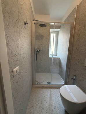 A modern bathroom with a glass-enclosed shower, a white bathtub, and a visible window.