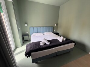 A hotel room with a bed, a nightstand, and a wall-mounted lamp.