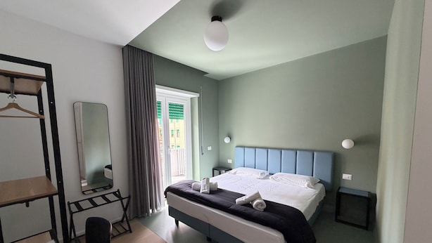 A bedroom with a bed, bedside tables, a mirror, a wardrobe, and a door leading to an outdoor balcony. - Luciano King's Guest House (Roma)