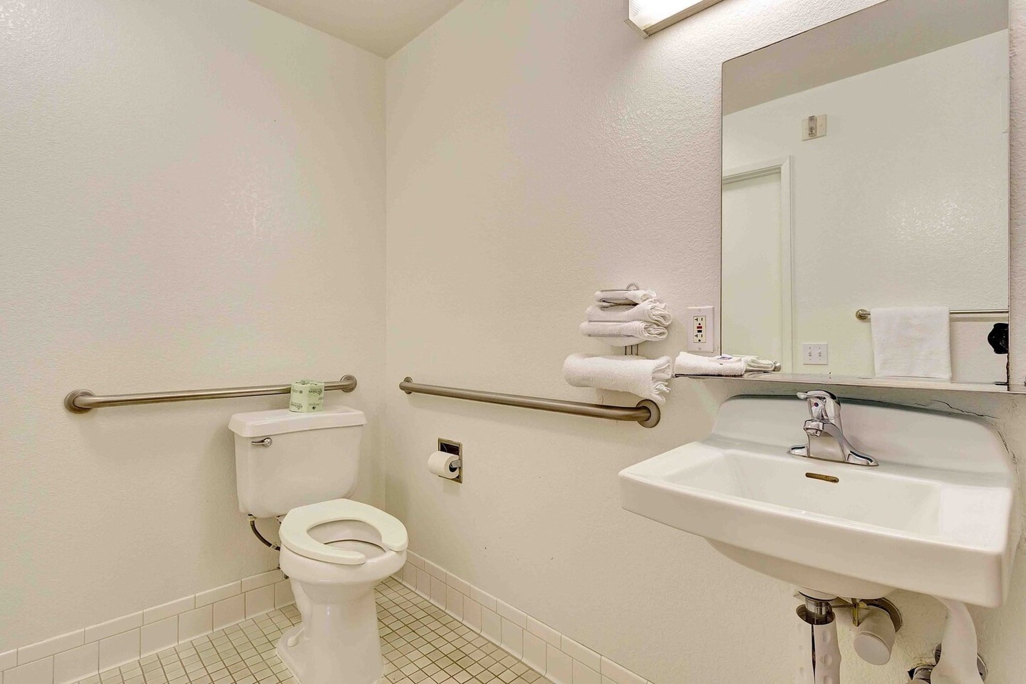 A standard hotel bathroom with a toilet, a sink, a mirror, and a towel rack.