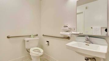 A standard hotel bathroom with a toilet, a sink, a mirror, and a towel rack.