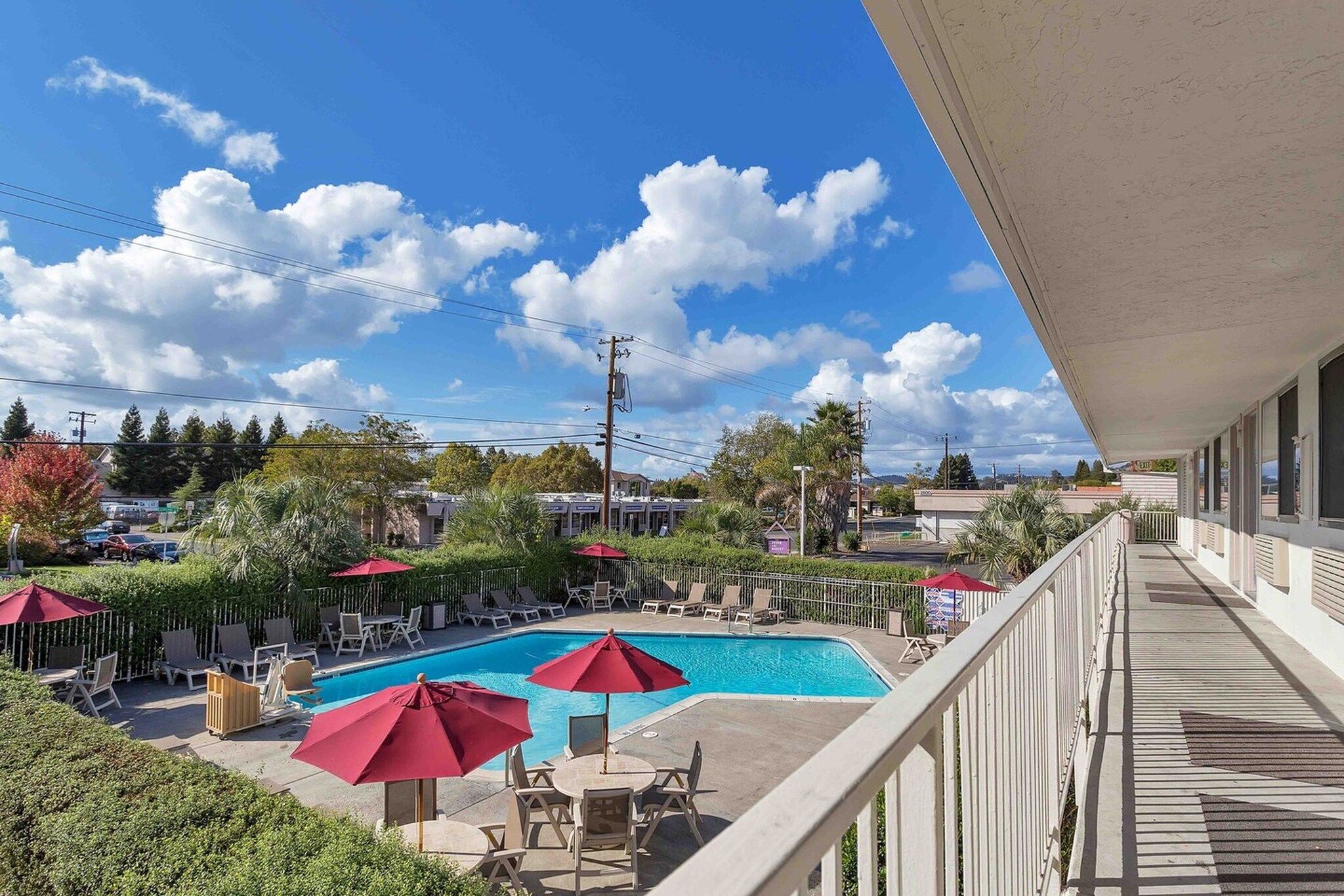 A pool area with lounge chairs and umbrellas, overlooking a residential neighborhood with houses and trees.