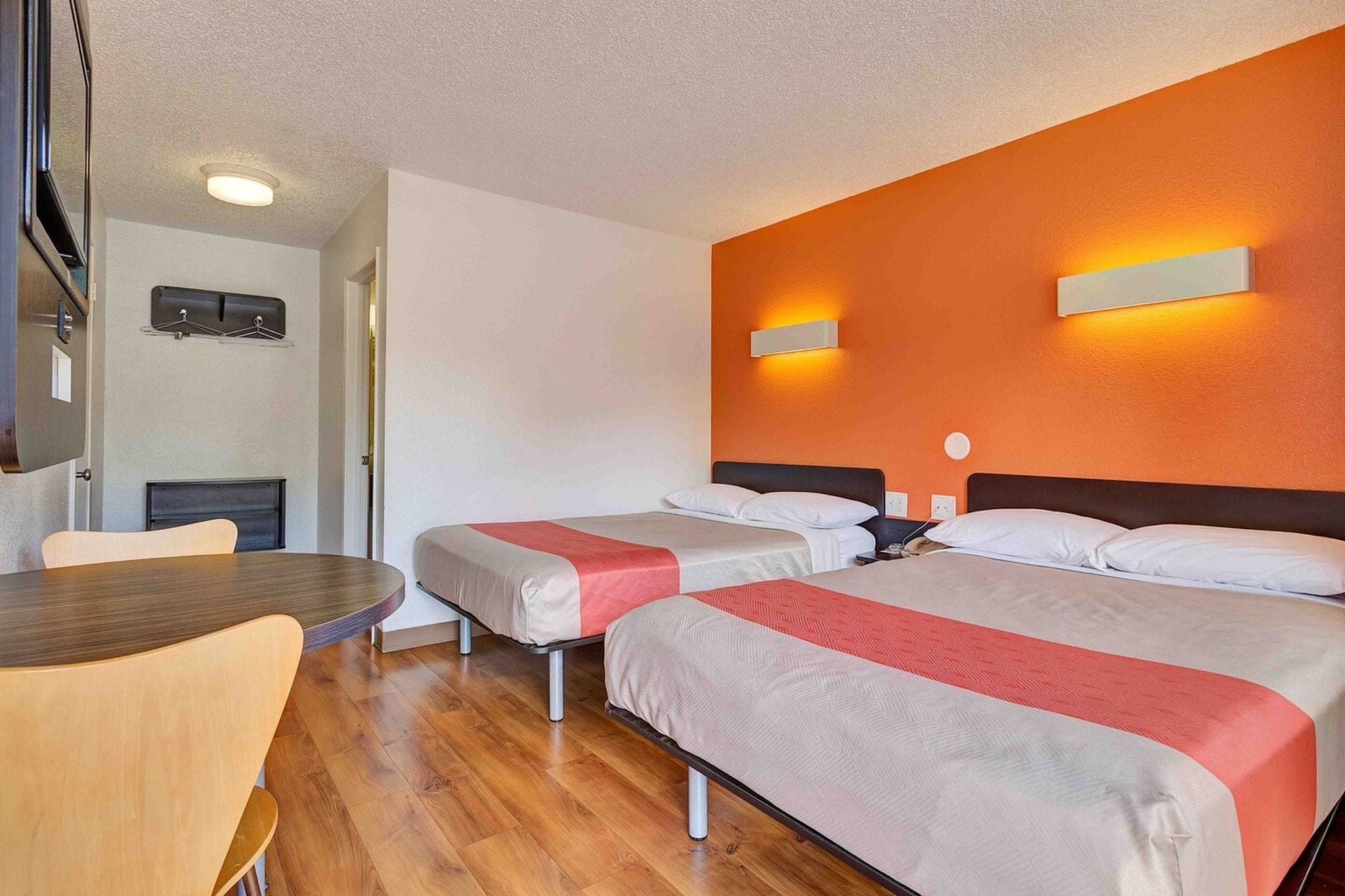 Une chambre d’hôtel avec deux lits, une table en bois et un luminaire fixé au mur.