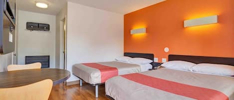 A hotel room with two beds, a wooden table, and a wall-mounted light fixture.
