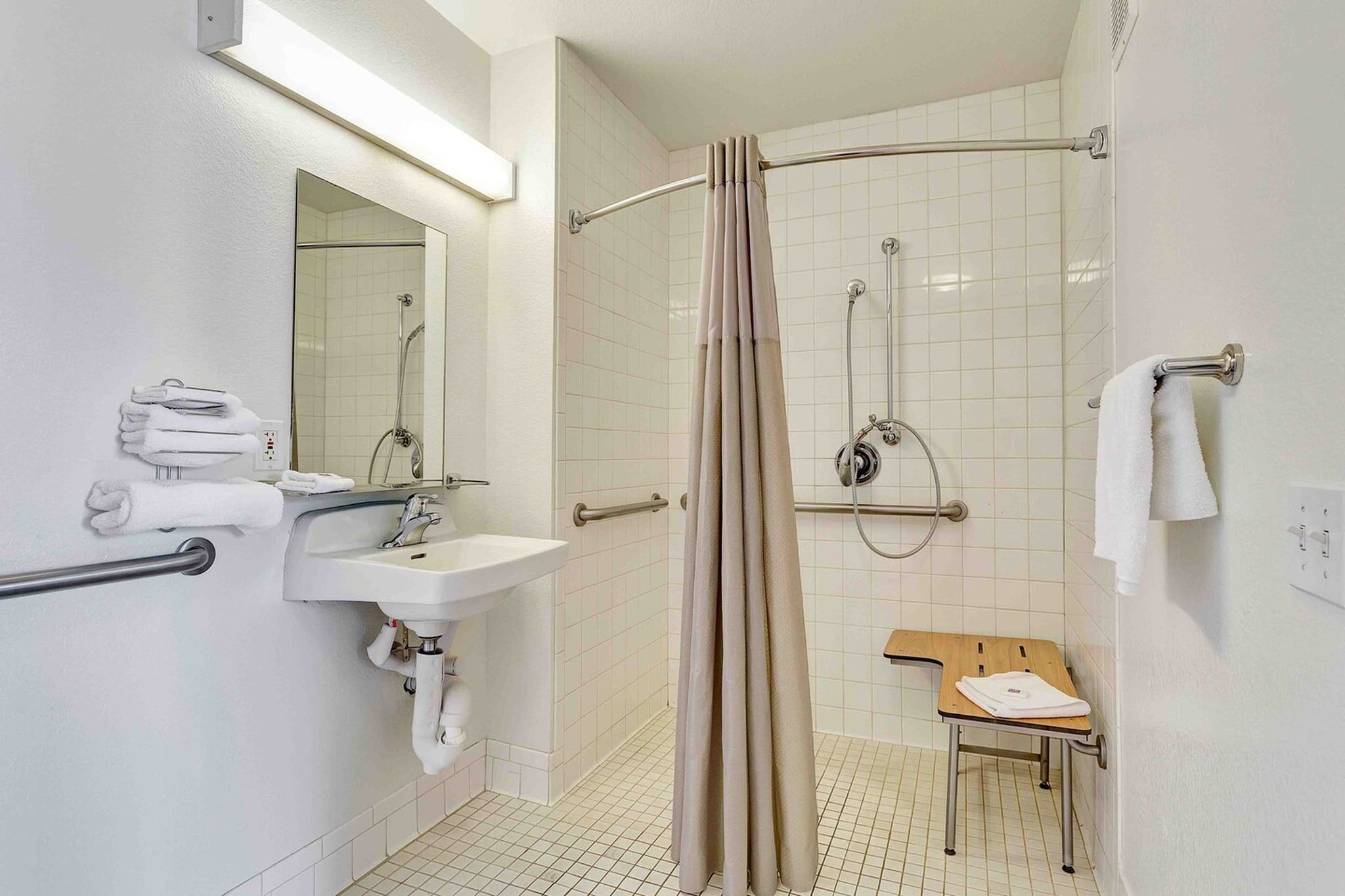 A bathroom with a sink, mirror, shower, and a wooden bench.