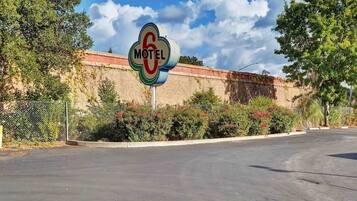 A motel sign with a number 6, surrounded by greenery and a brick wall.