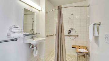 A bathroom with a sink, mirror, shower, and a wooden bench.