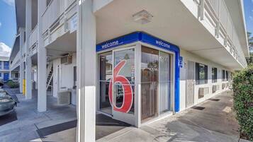 A building with a 'Welcome' sign, a large number '6' sign, and a parking area with a 'Register Parking Only' sign.