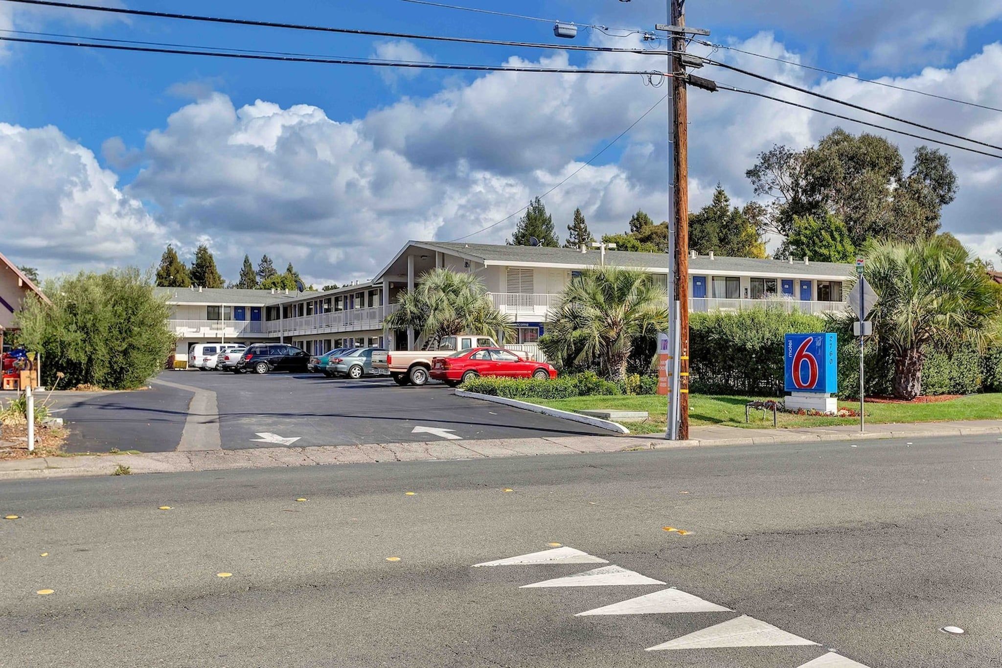 A motel with a parking lot, a red car parked in front, and a signboard.