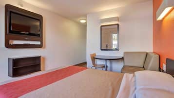 A hotel room with a bed, a desk, a chair, a television, and a mirror.