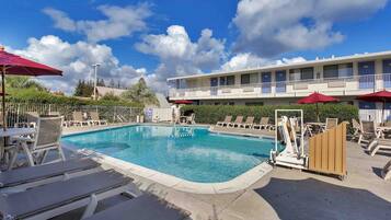 A swimming pool with lounge chairs and umbrellas, surrounded by a building with multiple balconies.