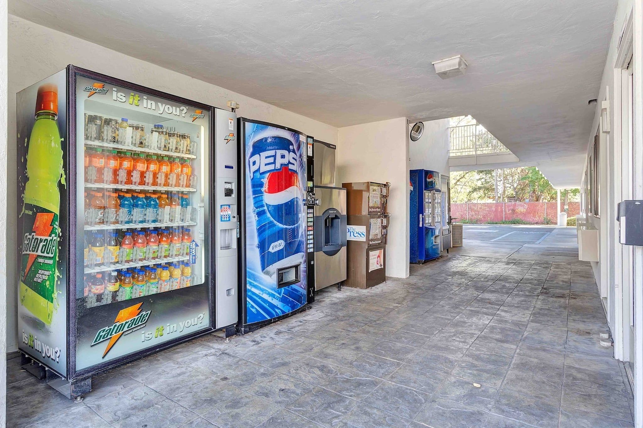 A corridor with vending machines, including a Gatorade cooler and a Pepsi cooler, and a newspaper dispenser.