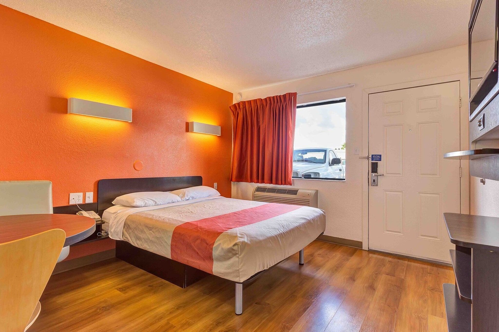 Une chambre d’hôtel avec un lit, une table de chevet, une lampe et une fenêtre avec des rideaux.