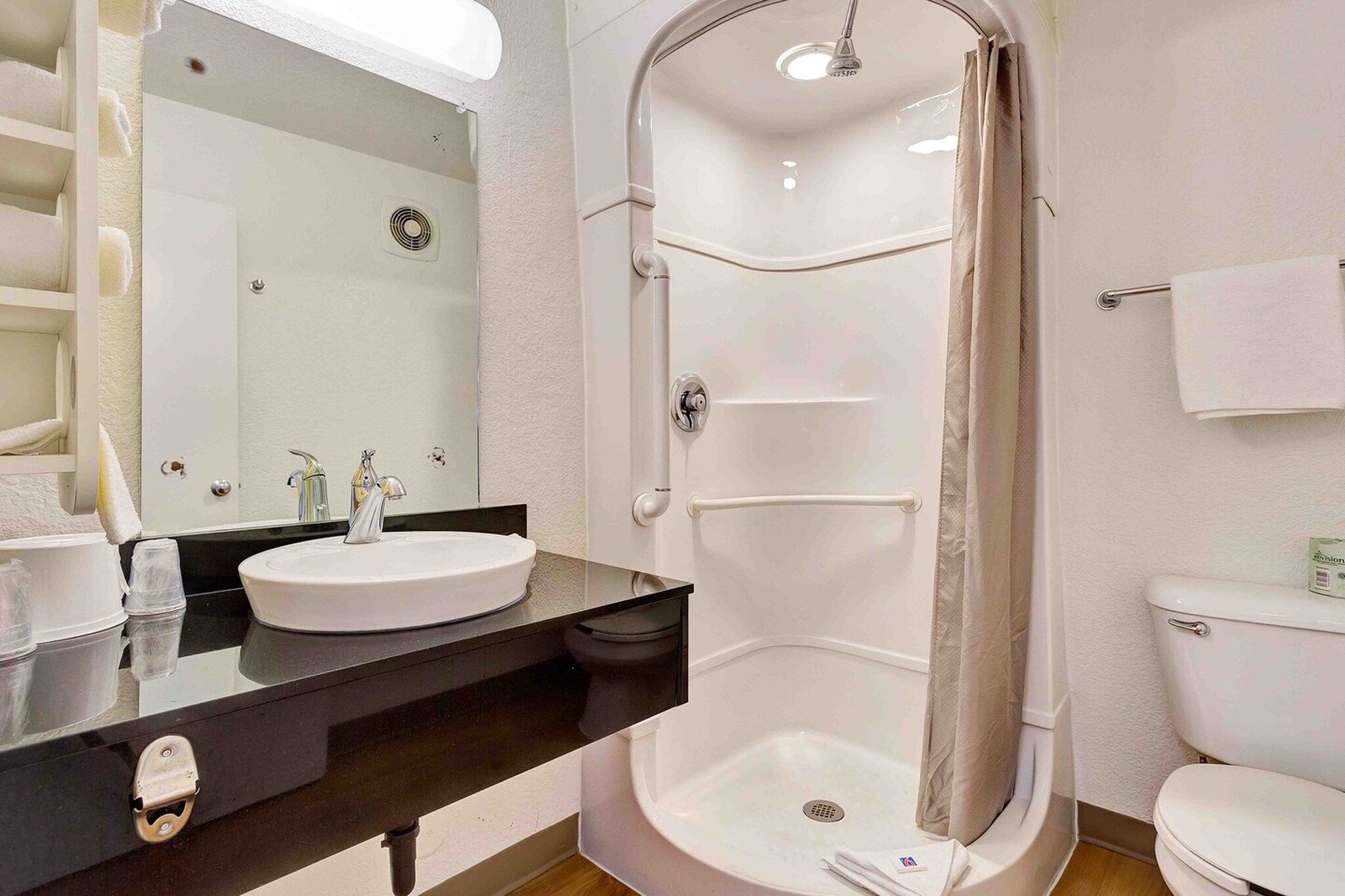 Une salle de bain moderne avec un lavabo blanc, un plan de toilette noir, une douche à parois de verre et des toilettes.