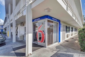 A building with a 'Welcome' sign, a large number '6' sign, and a parking area with a 'Register Parking Only' sign.