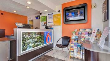 A hotel reception area with a counter, a television mounted on the wall, and a display of travel brochures.