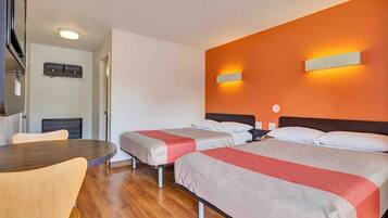 A hotel room with two beds, a wooden table, and a wall-mounted light fixture.