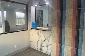A bathroom with a marble wall, a mirror, and a colorful striped tile accent.