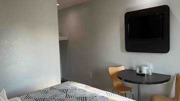 Ein Hotelzimmer mit einem Bett, einem kleinen Tisch, zwei Stühlen und einem an der Wand befestigten Fernseher.