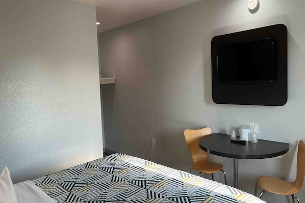 A hotel room with a bed, a small table, two chairs, and a TV mounted on the wall.