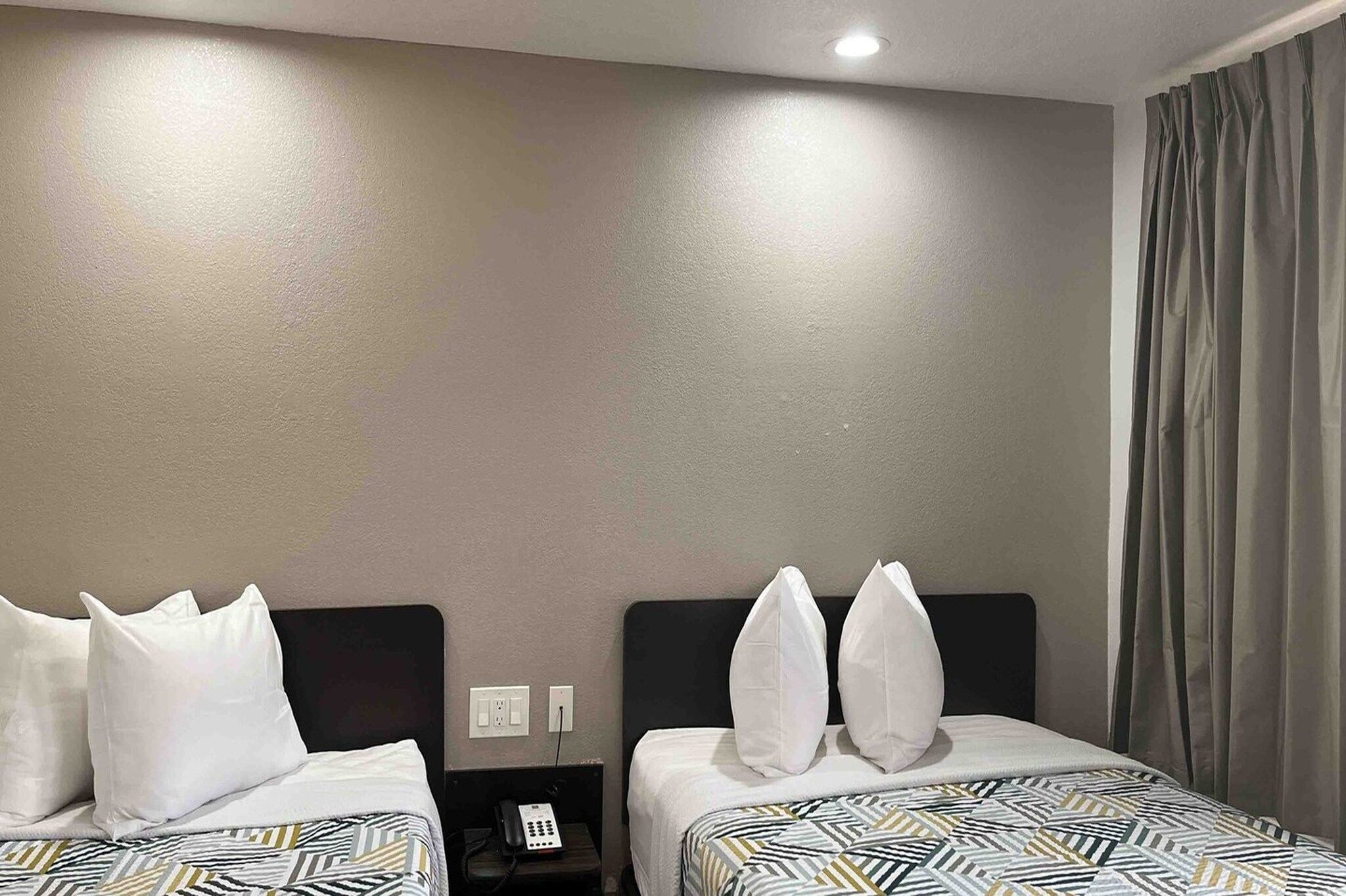 A hotel room with two beds, each with patterned bedding and white pillows. There is a nightstand with a phone between the beds.