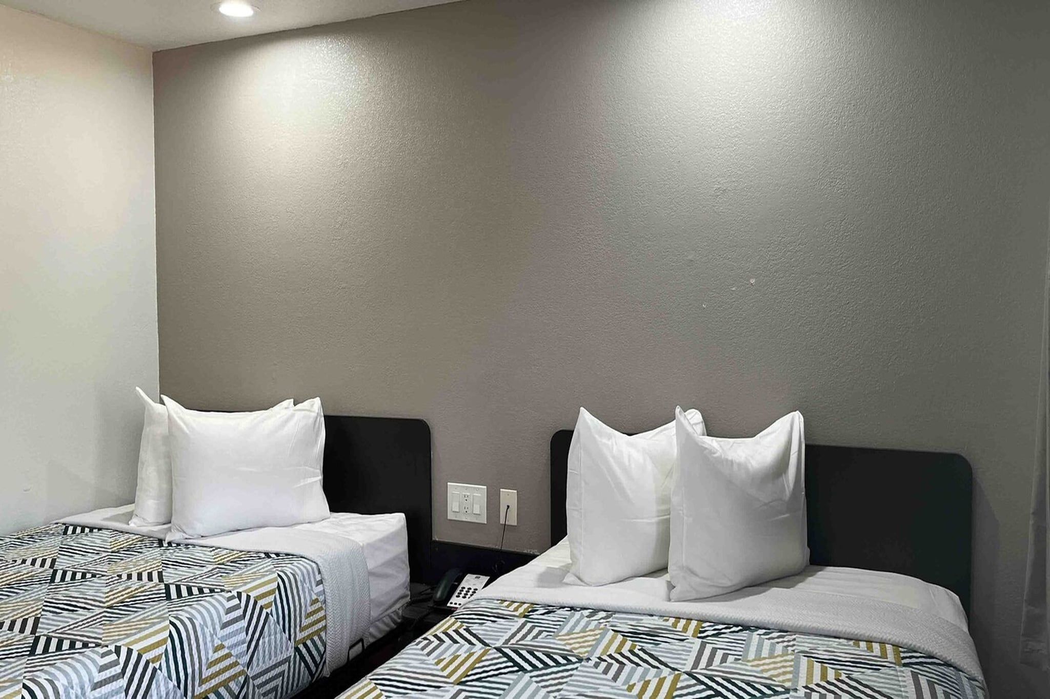 A hotel room with two beds, each with a patterned bedspread and white pillows.