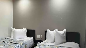 A hotel room with two beds, each with a patterned bedspread and white pillows.
