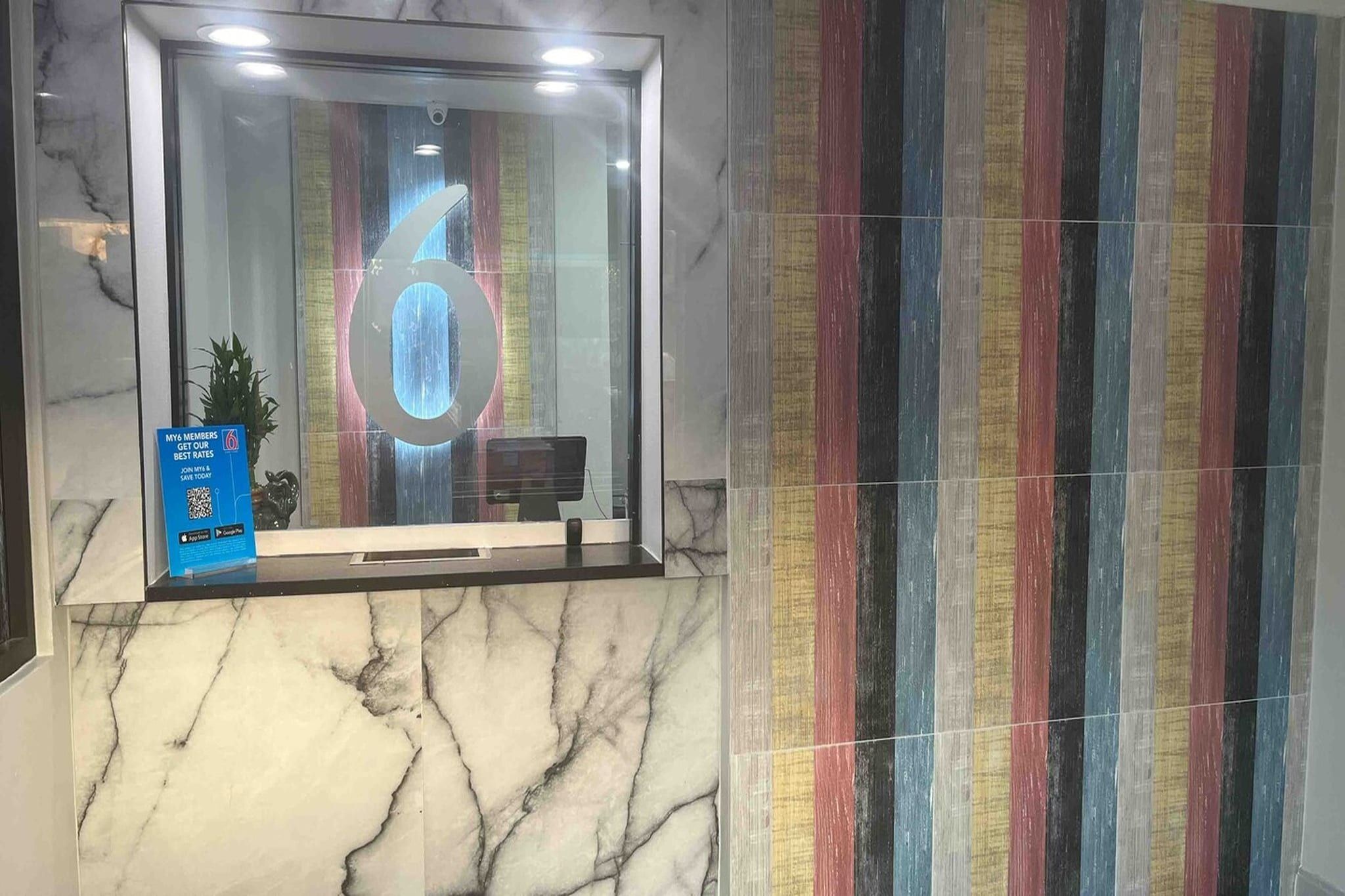 A reception area with a marble wall, a glass door with a number '6' reflected, and a colorful striped wall.
