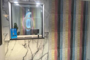 Un área de recepción con piso de mármol, una puerta de cristal que refleja el número '6' y una pared con rayas de colores.