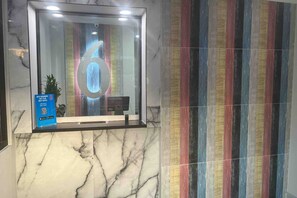 Una zona de recepción con suelo de mármol, una puerta de cristal con el número '6' iluminado y una pared de rayas coloridas.