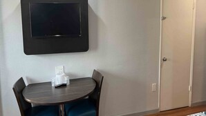 Quarto com mesa redonda, duas cadeiras, TV de tela plana na parede e porta fechada.