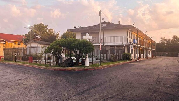 Um edifício de dois andares com portão fechado, estacionamento e céu aberto.