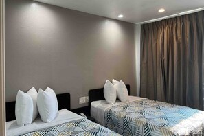 A hotel room with two beds, each with a patterned bedspread, white pillows, and a dark headboard.