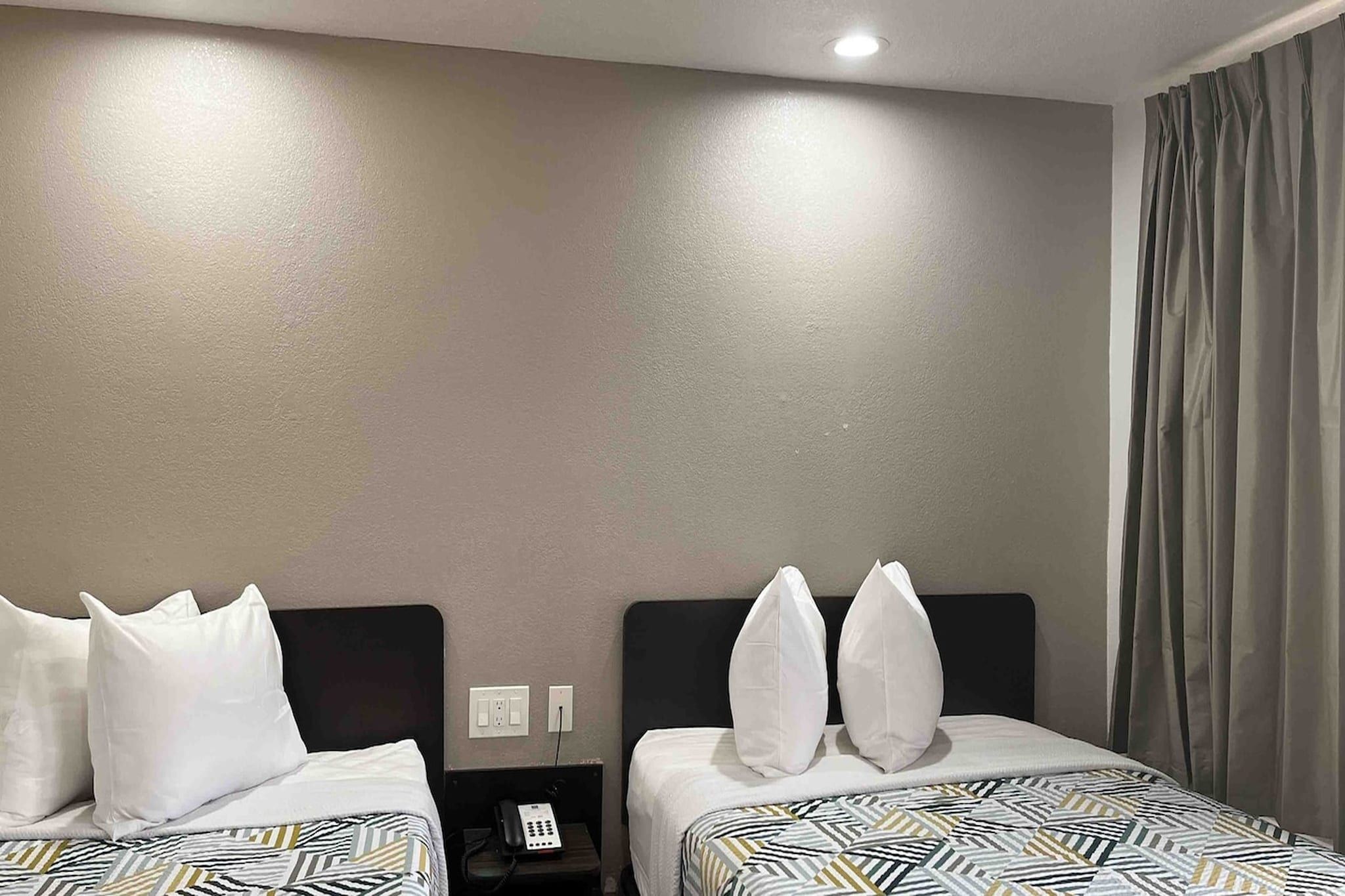 A hotel room with two beds, a nightstand with a phone, and a window with curtains.