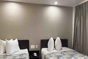 A hotel room with two beds, a nightstand with a phone, and a window with curtains. - 2 Full Beds | Non-Smoking (Dallas)