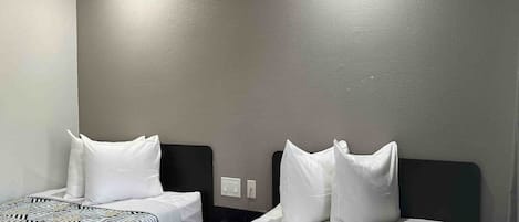 Two single beds with patterned bedding in a room with plain walls and a ceiling light.