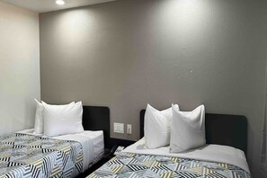 Two single beds with patterned bedding in a room with plain walls and a ceiling light.