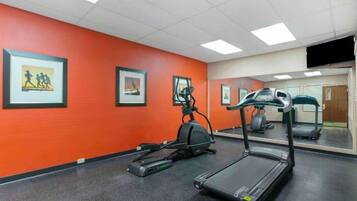 A gym with exercise equipment, a mirrored wall, and framed pictures on the orange wall.