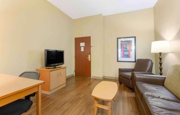 A furnished living room with a television, a sofa, a chair, a table, and a lamp.